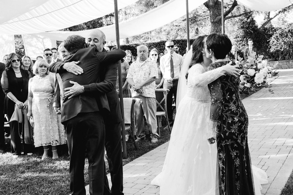 groom hugs father of the bride during charming wedding ceremony at Maravilla Gardens