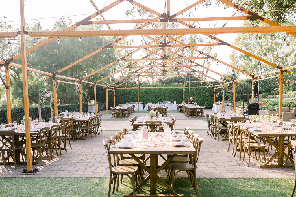 charming open air wedding reception at Maravilla Gardens under pergola with wooden farmhouse tables, chairs and pink accents