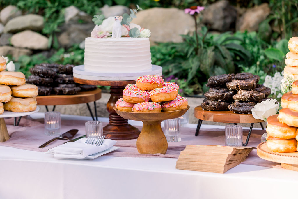 one tier wedding cake with figurine of couple's dog as cake topper surrounded by donuts