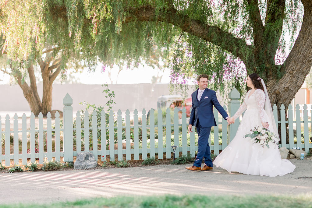 bride in long sleeve wedding dress with floral lace appliqué and sweetheart neckline stands with groom in blue suit and floral tie at Maravilla Gardens