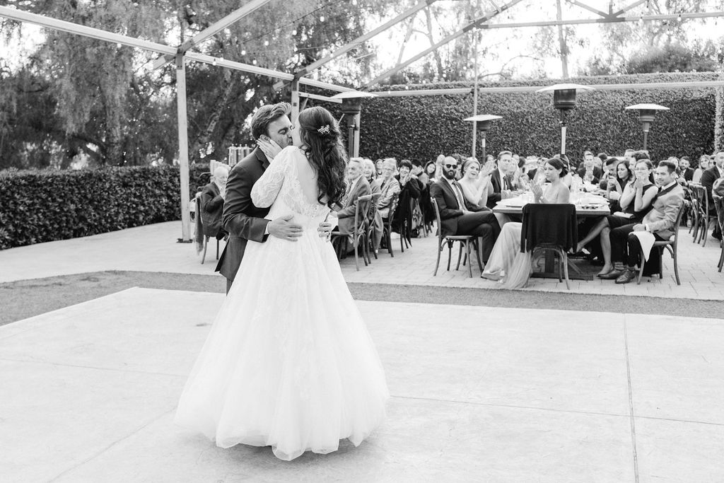 bride in long sleeve wedding dress walks with groom in blue suit have first dance during reception at Maravilla Gardens