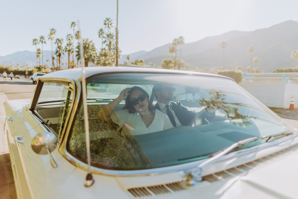 engaged couple poses with white vintage car during engagement photo session in Palm Springs