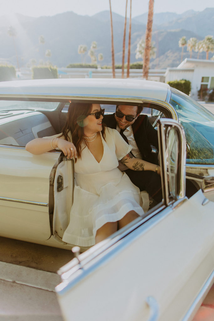 engaged couple poses with white vintage car during engagement photo session in Palm Springs