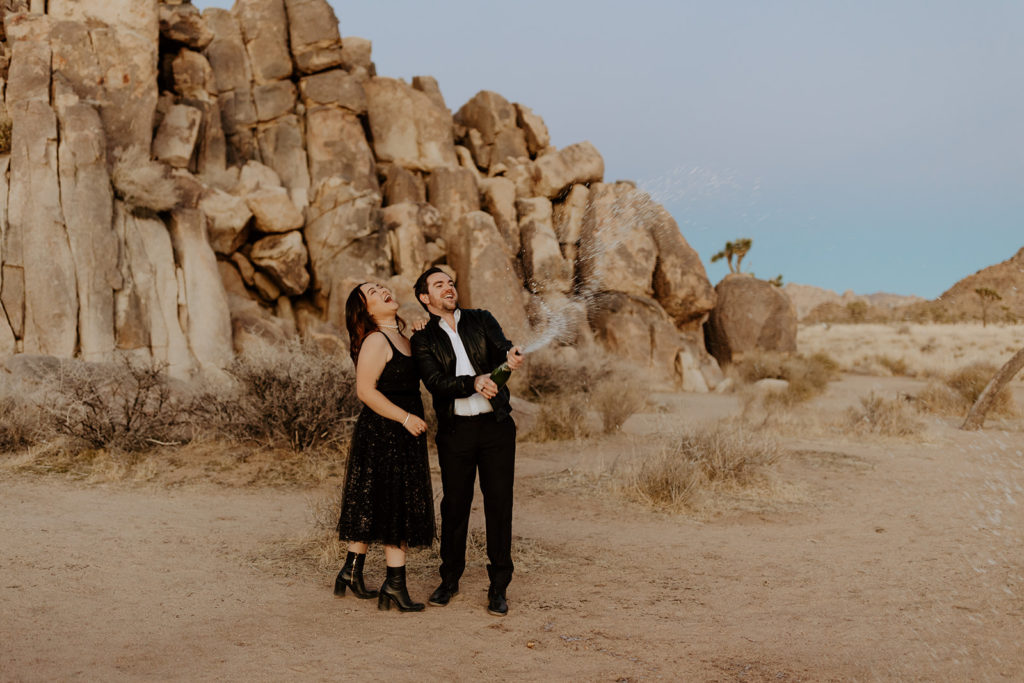 engaged couple in black outfits pose in Palm Spring desert for engagement photo session