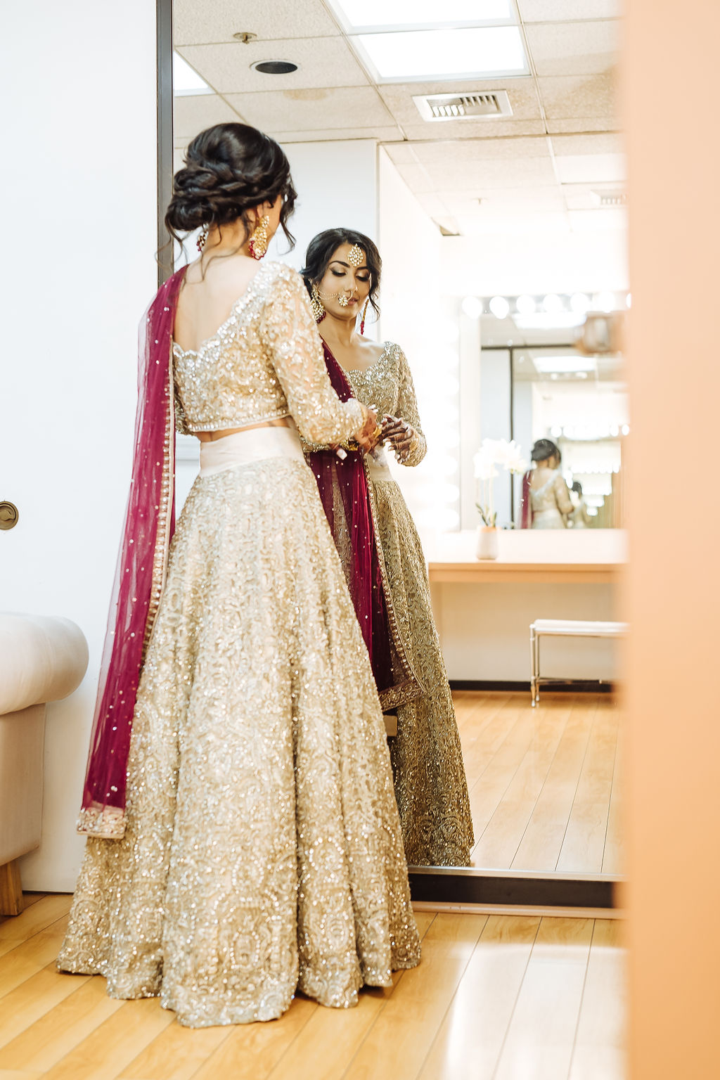 bride wearing embellished golden wedding saree puts on jewelry before wedding