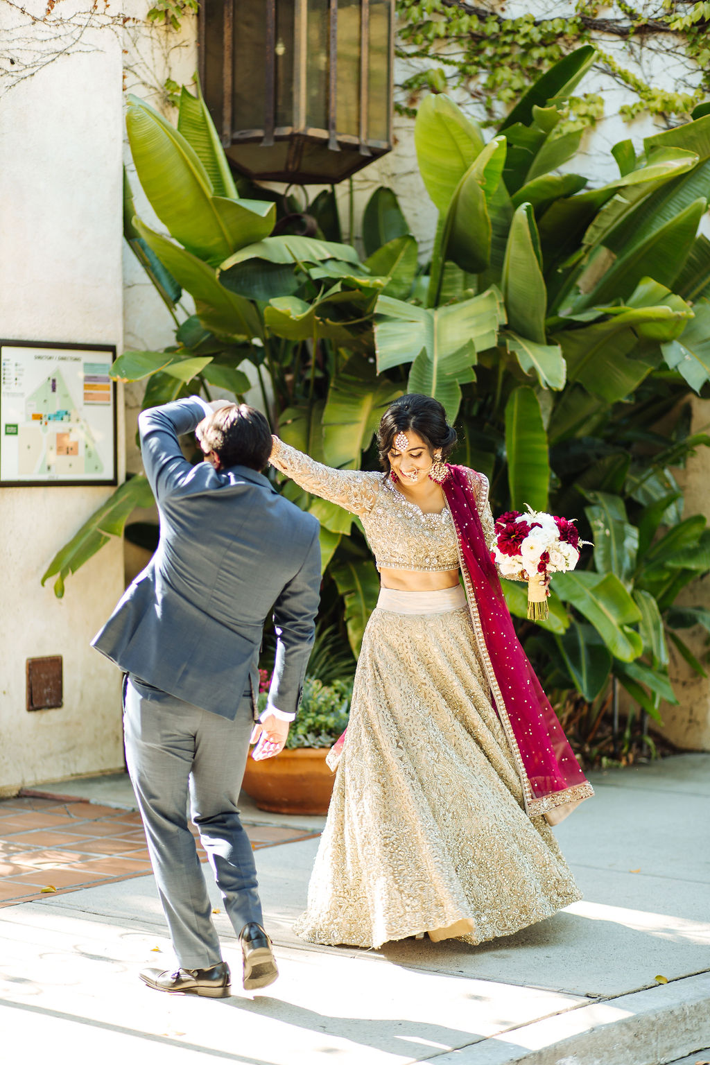 bride wearing embellished golden wedding saree and groom in dark grey suit with maroon tie dance at Los Angeles River and Garden Center