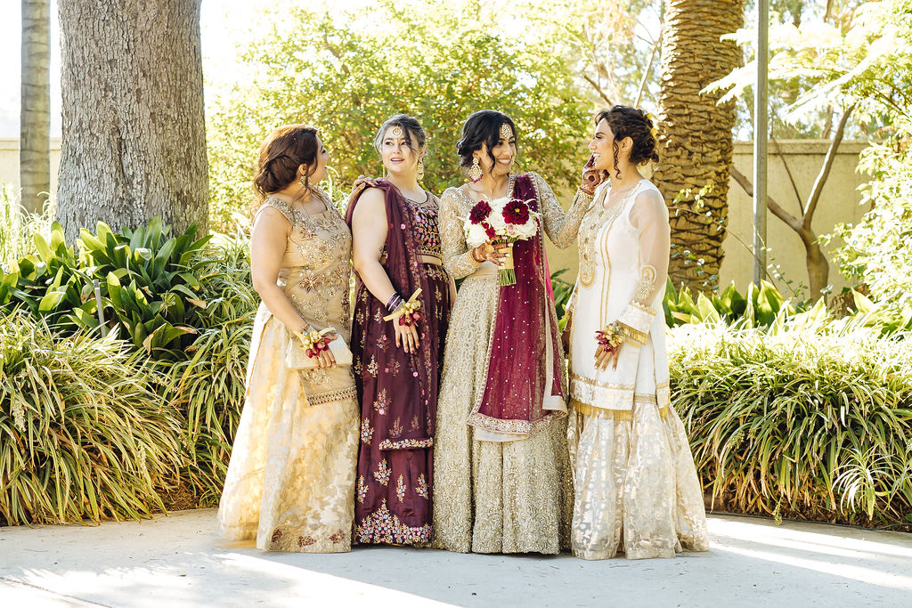 bride wearing embellished golden wedding saree stands with bridesmaids in gold and maroon saree