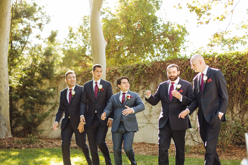 groom in dark grey suit and maroon tie walks with groomsmen in charcoal suits and maroon ties