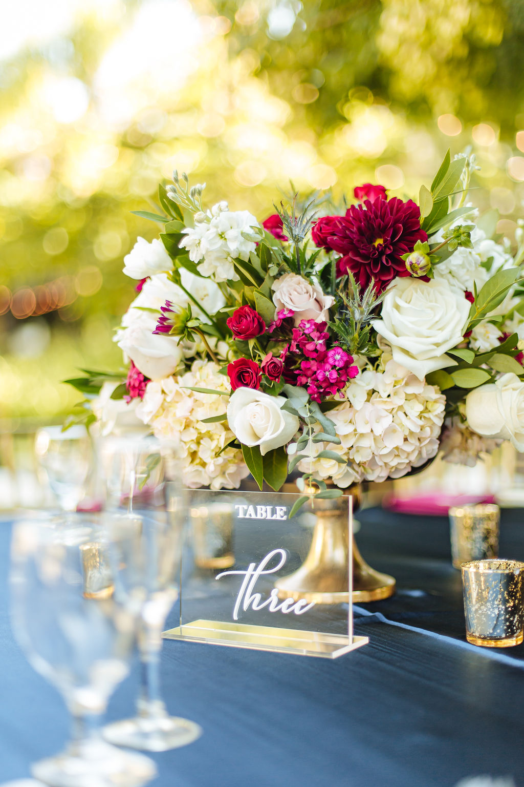 acrylic table number next to white and maroon floral arrangement in gold vase