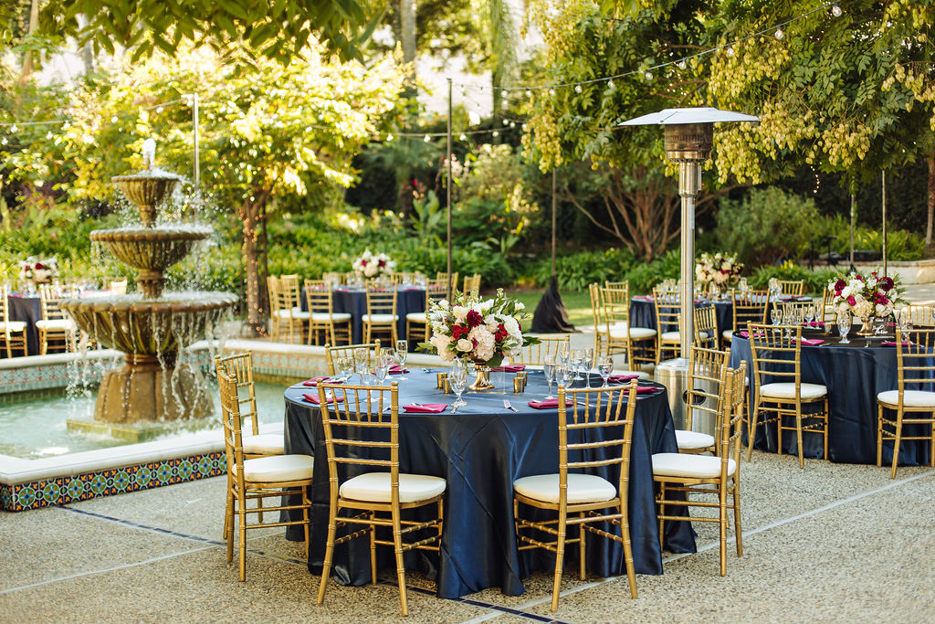 golden wedding reception at the Los Angeles River and Garden Center with gold chiavari chairs, silky black tablecloths and maroon and white floral arrangements
