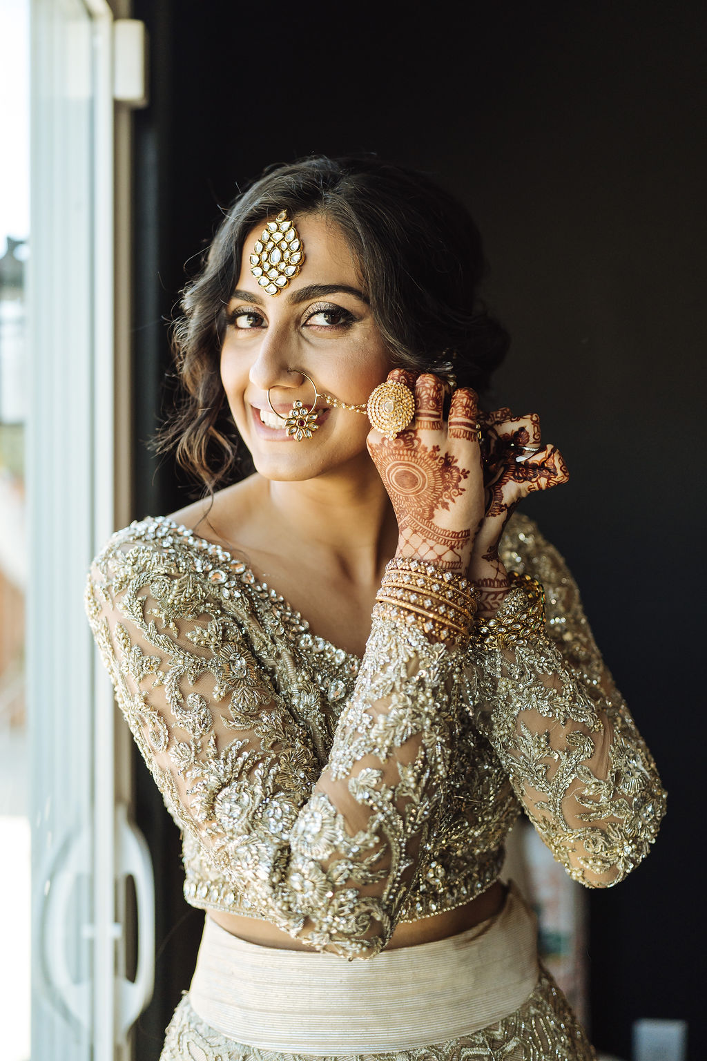 bride wearing golden wedding saree puts jewelry on before wedding