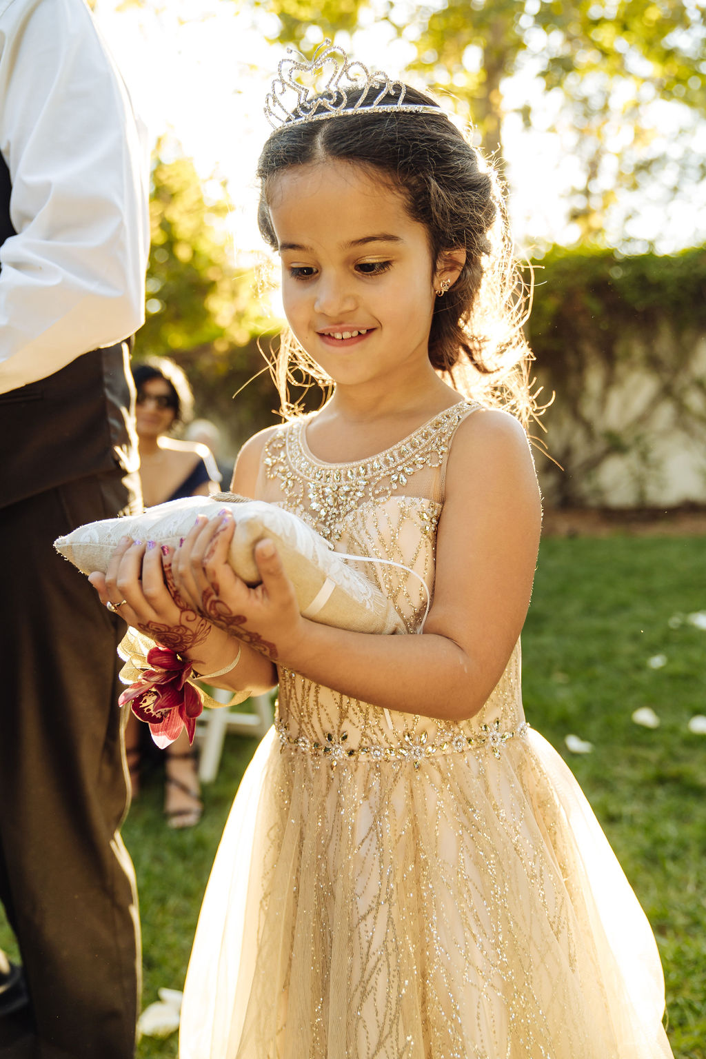 ring child wears gold dress and tiara while holding ring pillow down the aisle