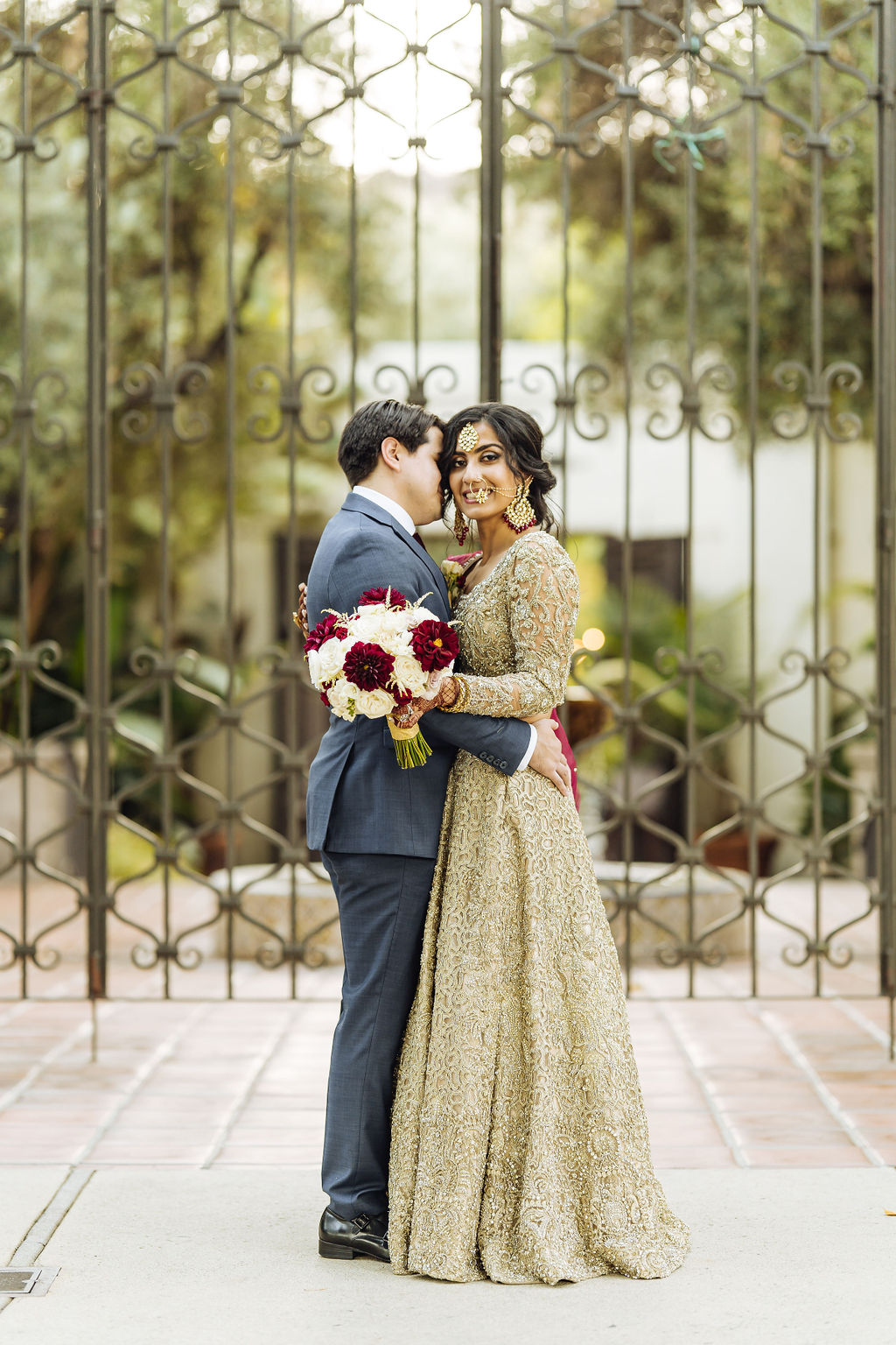 bride in embellished gold wedding saree with groom in dark grey suit and maroon tie take photos in the Los Angeles River Center and Gardens