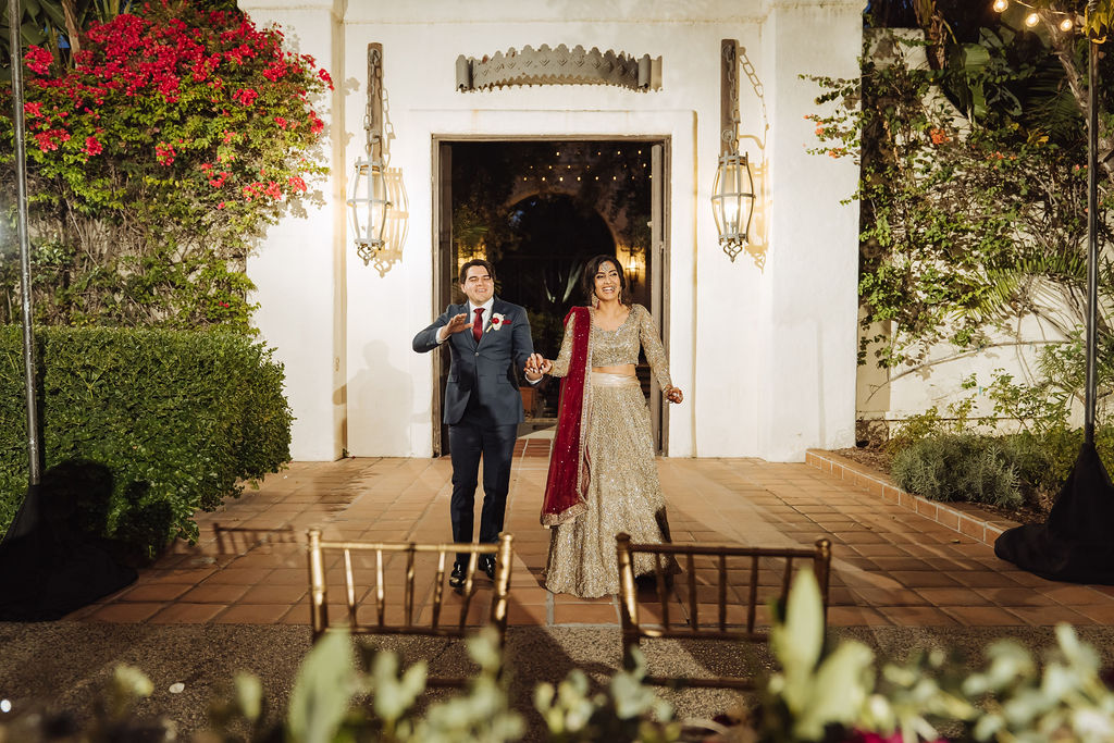 bride in embellished gold wedding saree with groom in dark grey suit and maroon tie walk into reception together