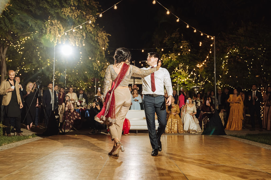 bride in embellished gold wedding saree with groom in dark grey suit and maroon tie have first dance