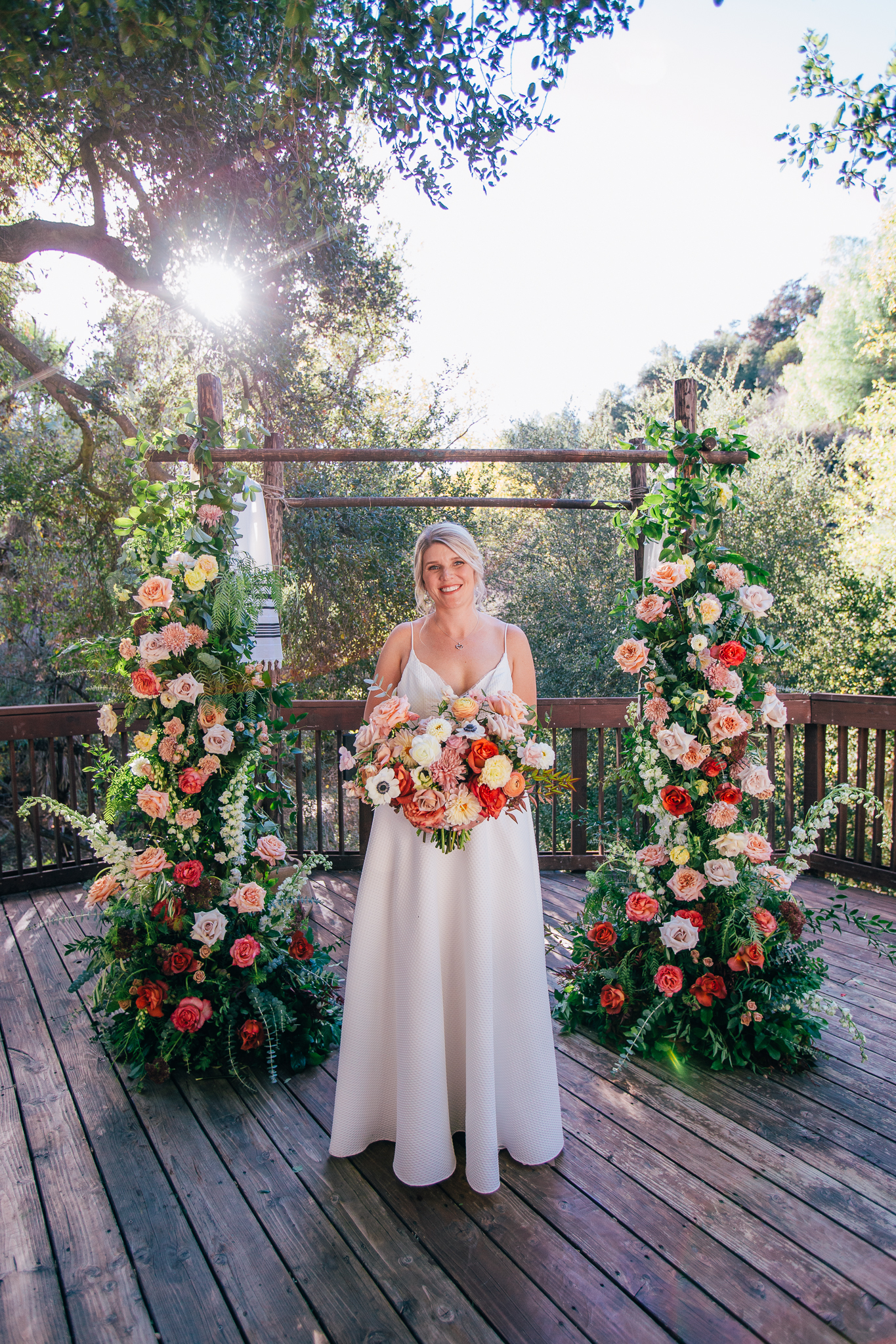 bride stands with bright and vibrant wedding bouquet in front of wedding ceremony arch with colorful florals