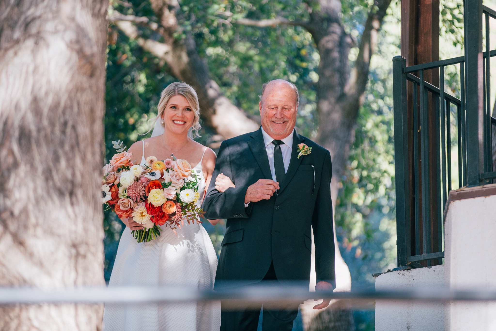 bride in spaghetti strap wedding dress and vibrant wedding bouquet walks with father down aisle