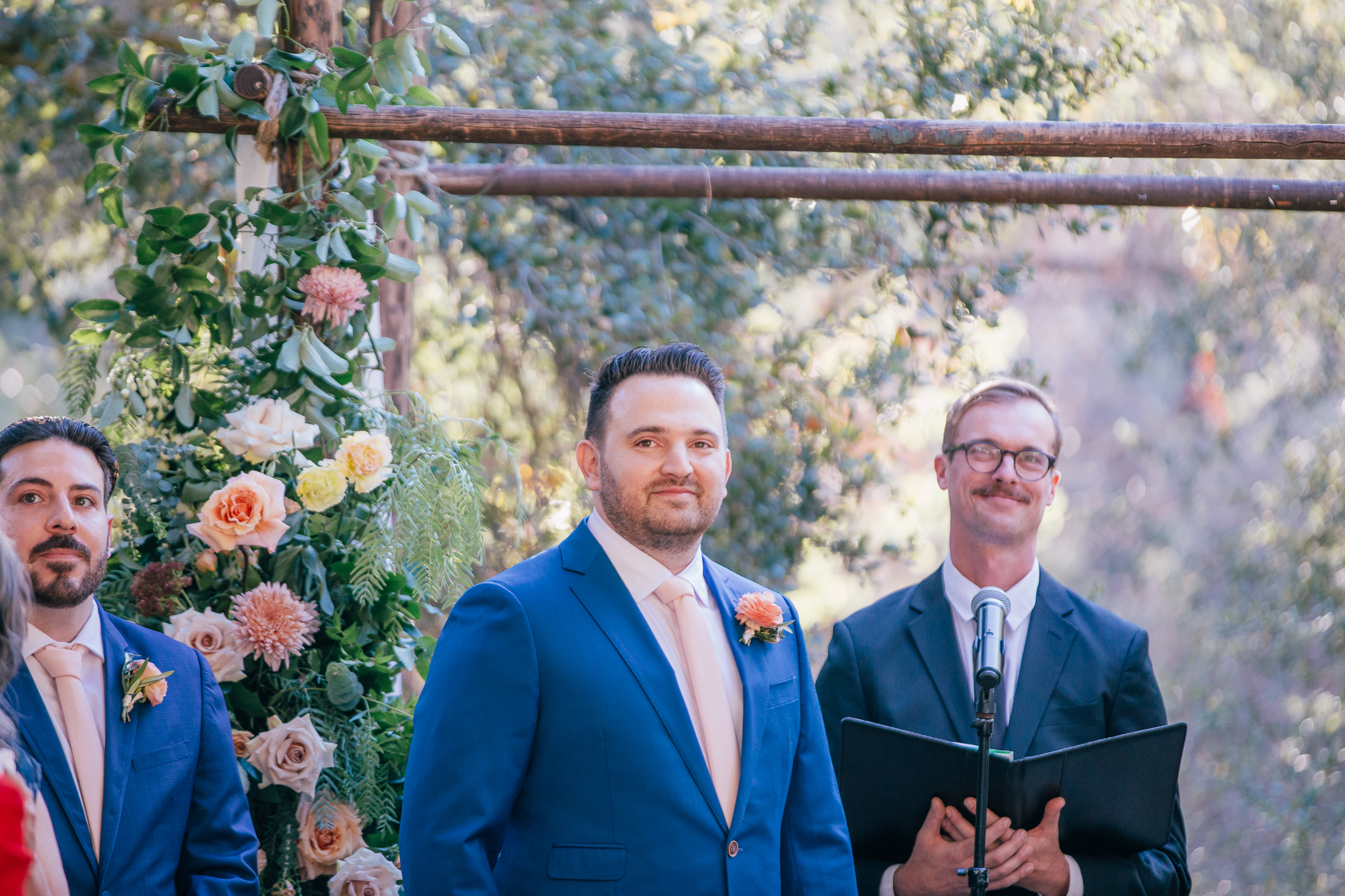 groom in blue suit and light pink tie sees bride walking down aisle