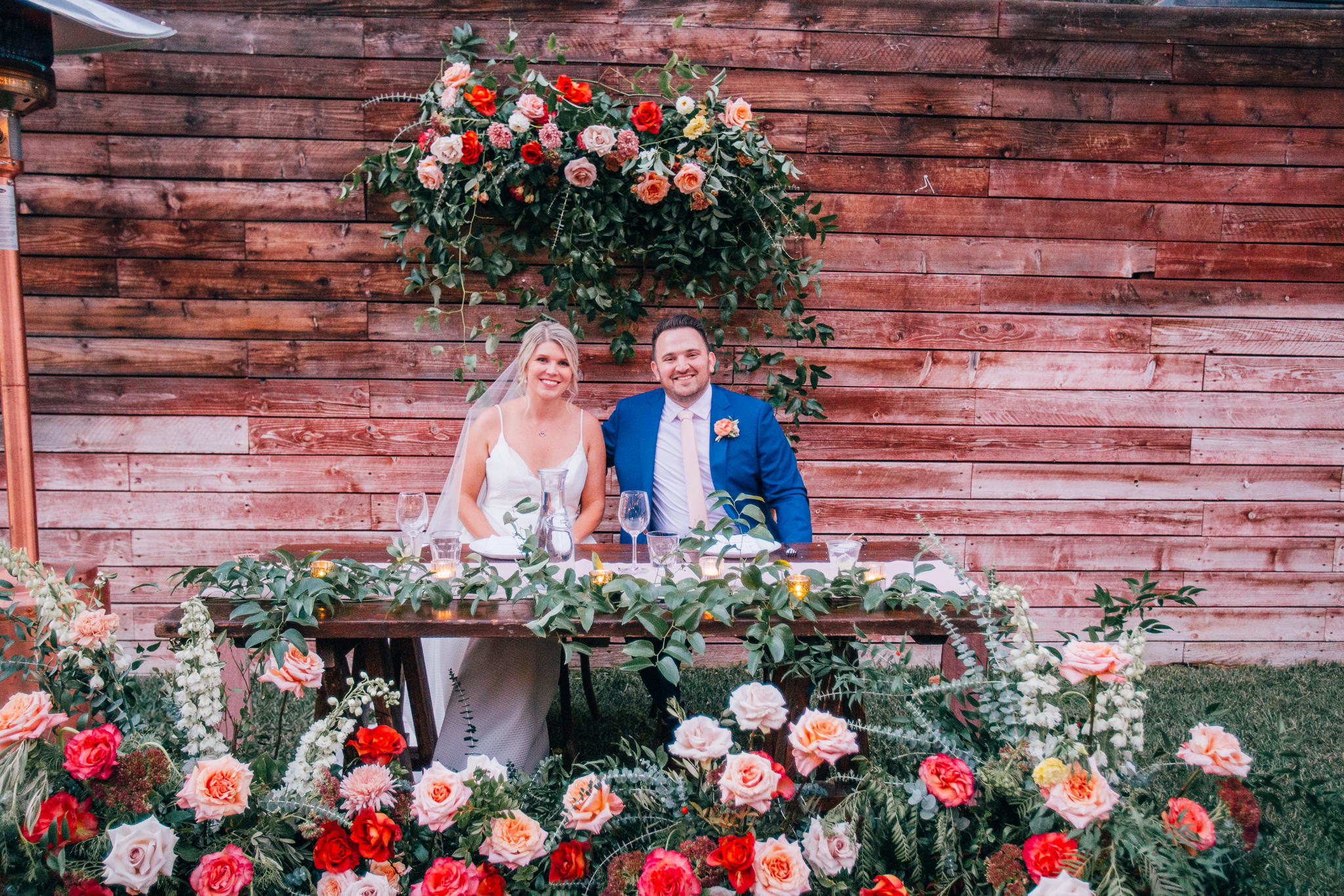 bride and groom at sweetheart table surrounded by bright and colorful florals