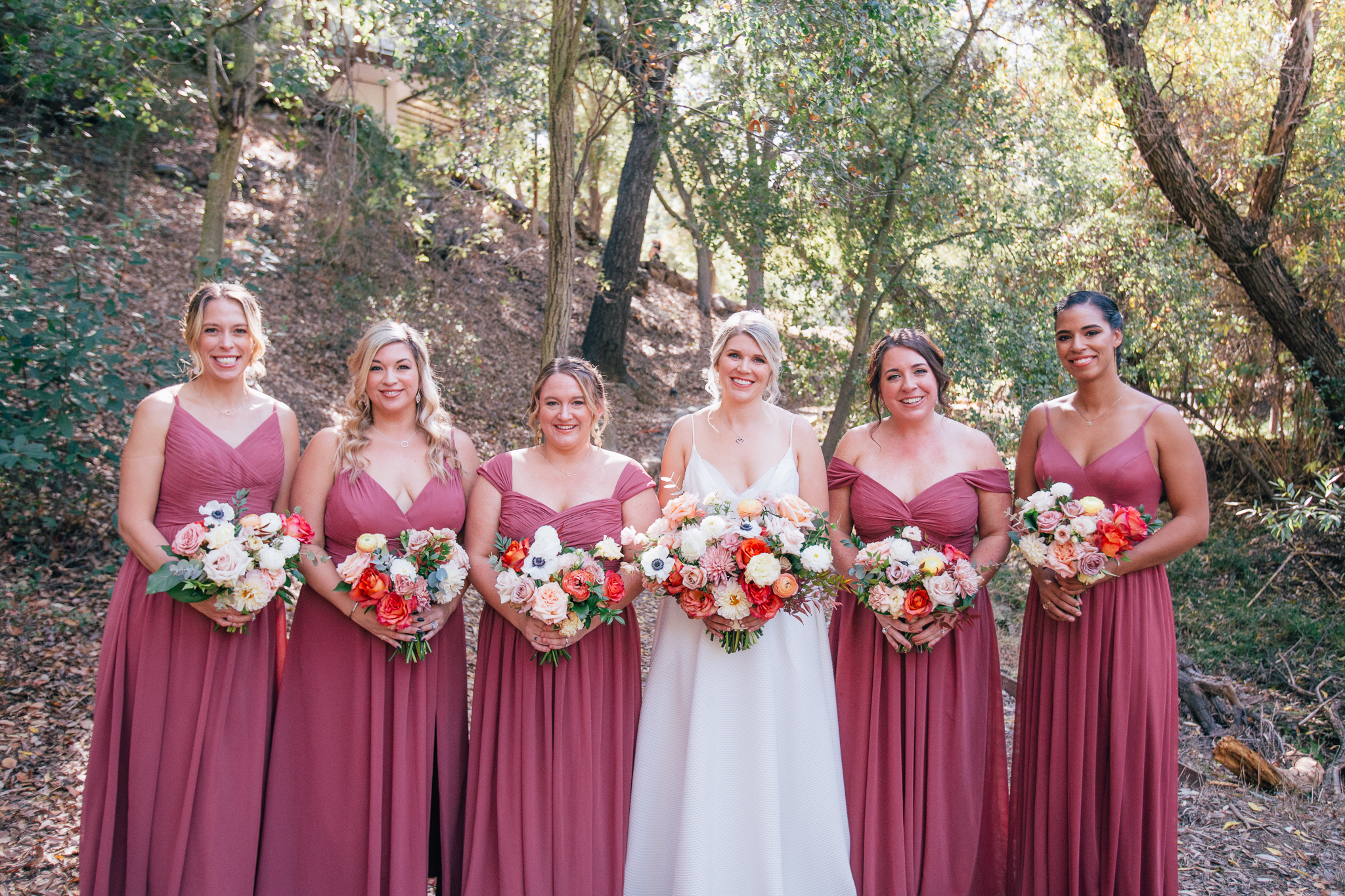 bride stands with bridesmaids in mauve dresses while holding bright and vibrant wedding bouquets