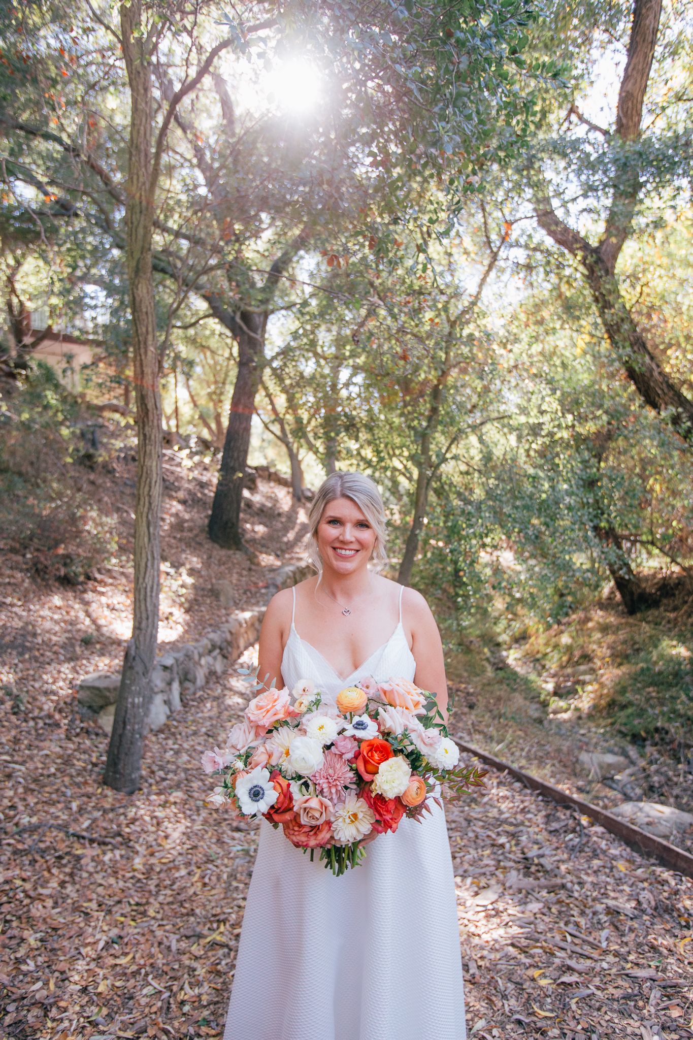 bride in spaghetti strap dress stands with bright and vibrant wedding bouquet with mixture of colorful flowers