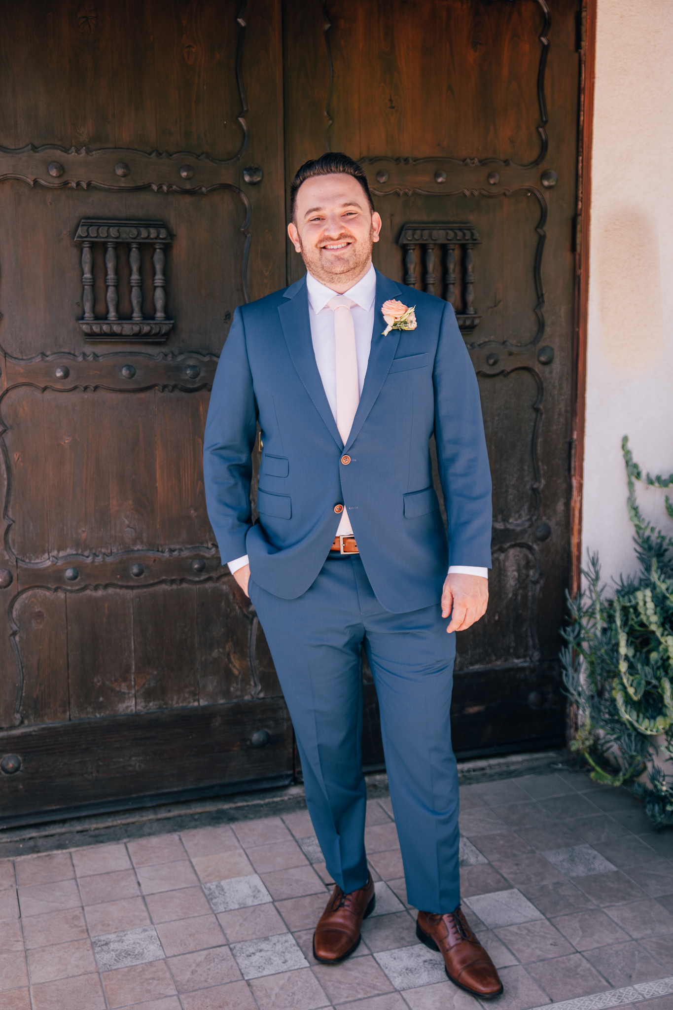 groom wearing blue suit with light pink tie gets ready for wedding
