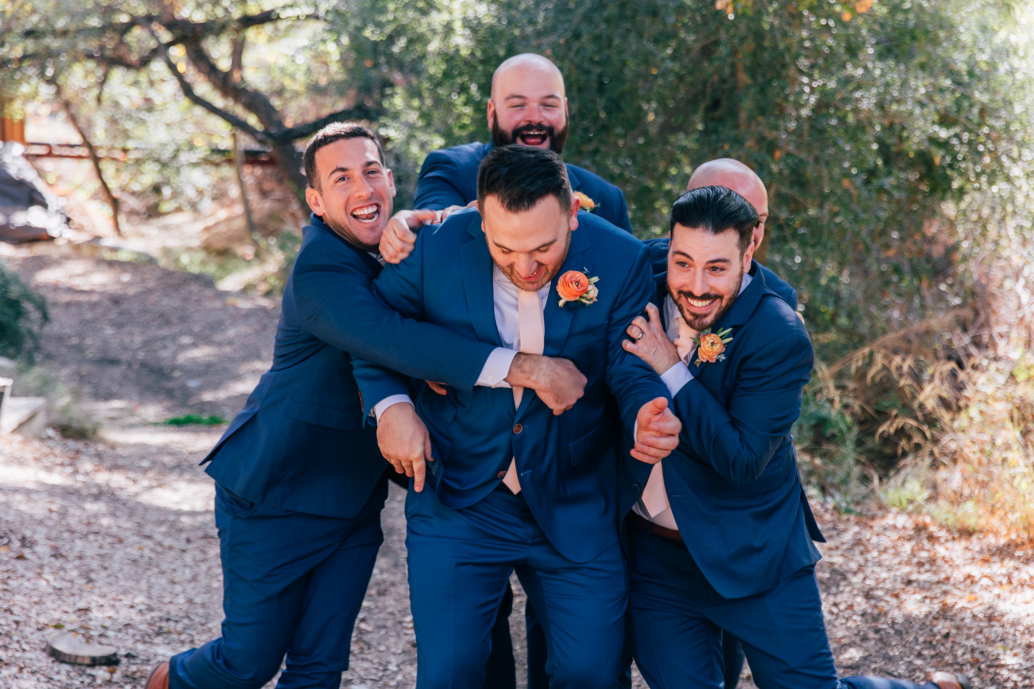 groom stands with groomsmen in blue suits with light pink ties and brown shoes