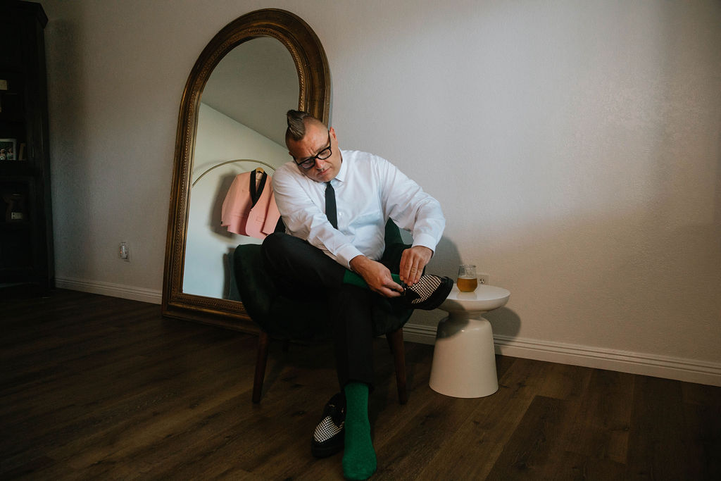 groom in green socks putting on houndstooth shoes