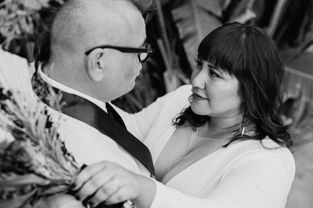 black and white photo of bride in long sleeve deep v-neck wedding dress holding a bouquet of dried florals with groom 