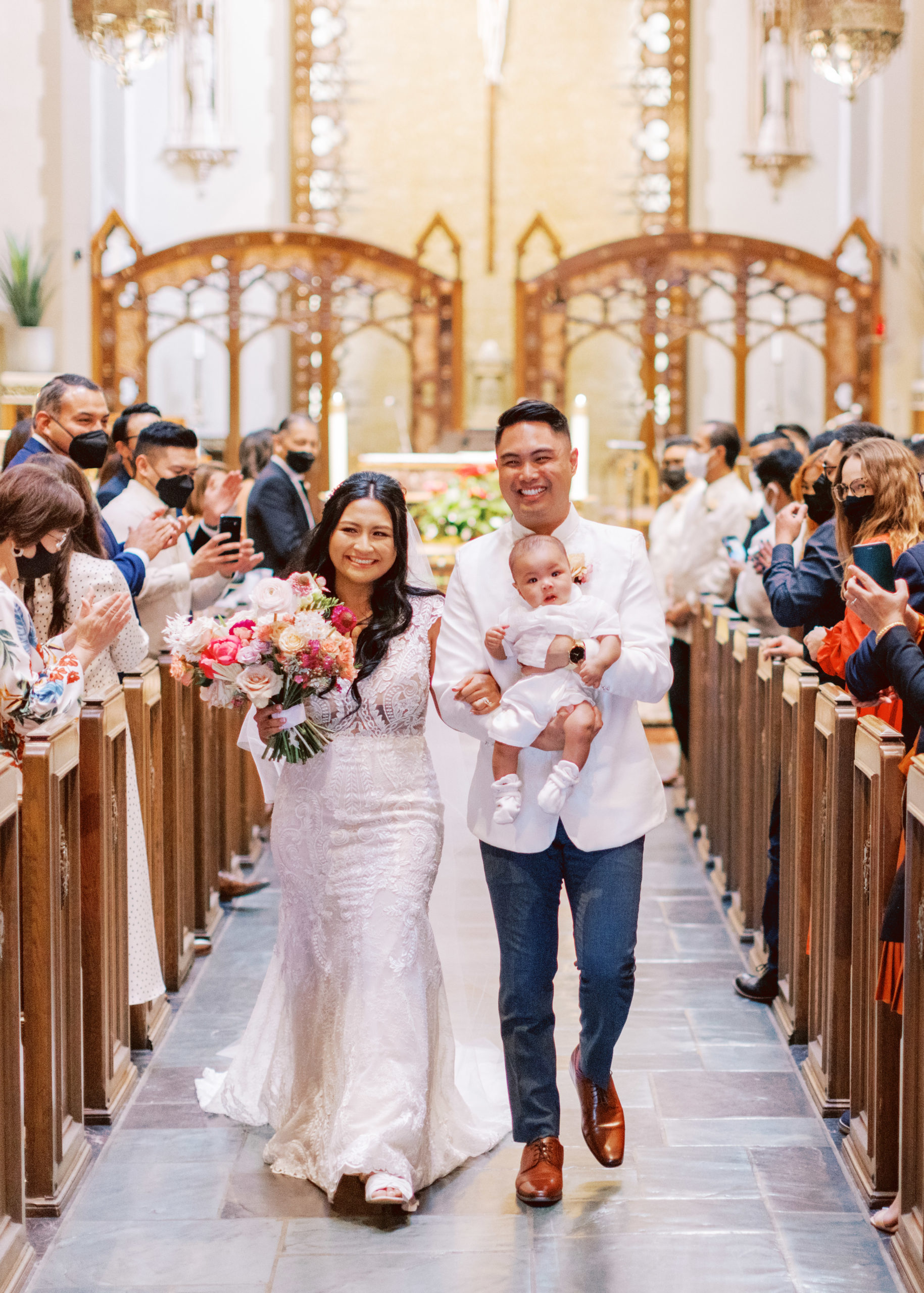 bride and groom hold their baby during their postponed wedding ceremony while walking down the altar