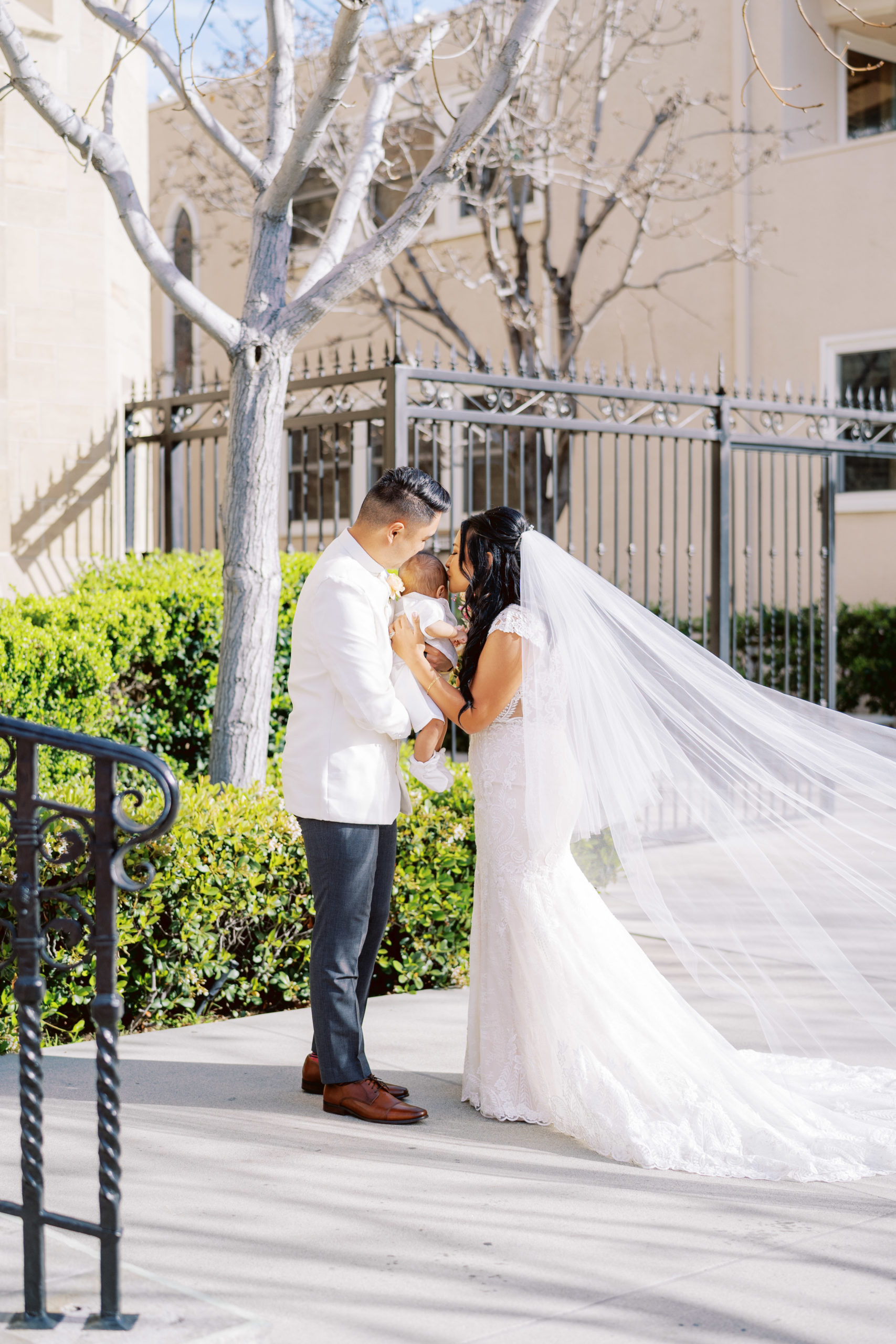 bride and groom kiss baby during wedding portrait shots