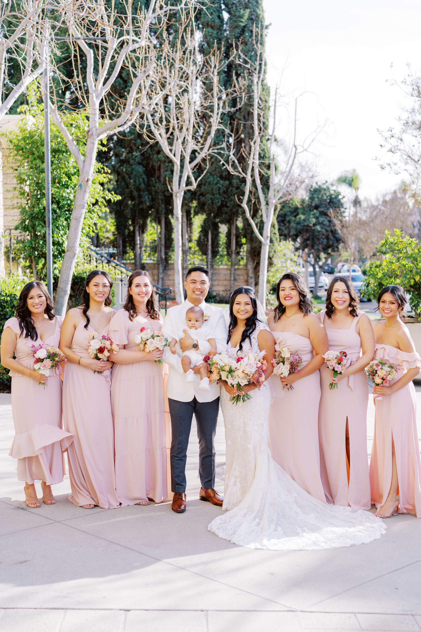 bride and groom stand with bridesmaids in mix matched soft pink dresses