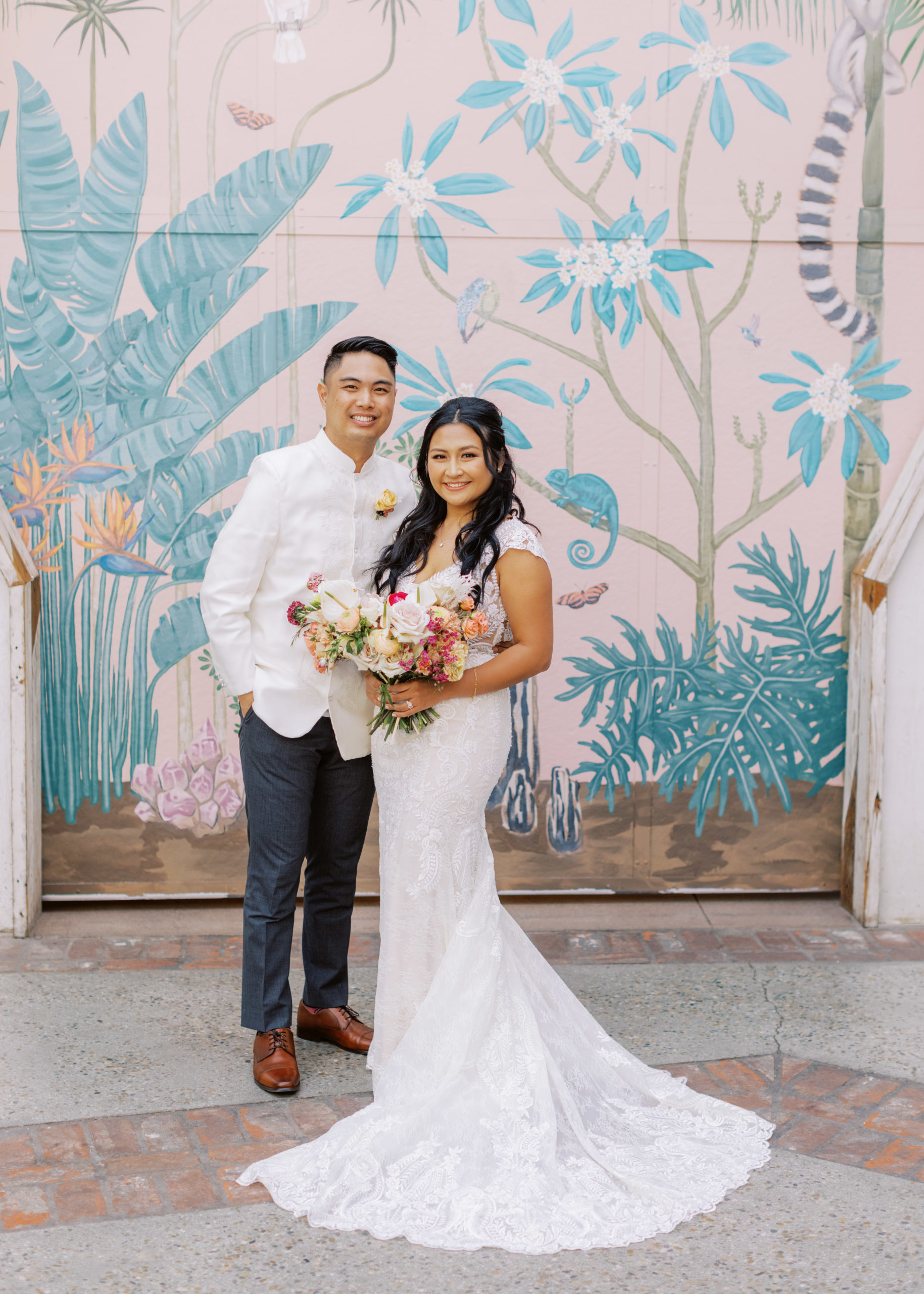 bride in lace dress holding tropical bouquet and groom in white wedding attire pose during cocktail hour at The Valentine DTLA 