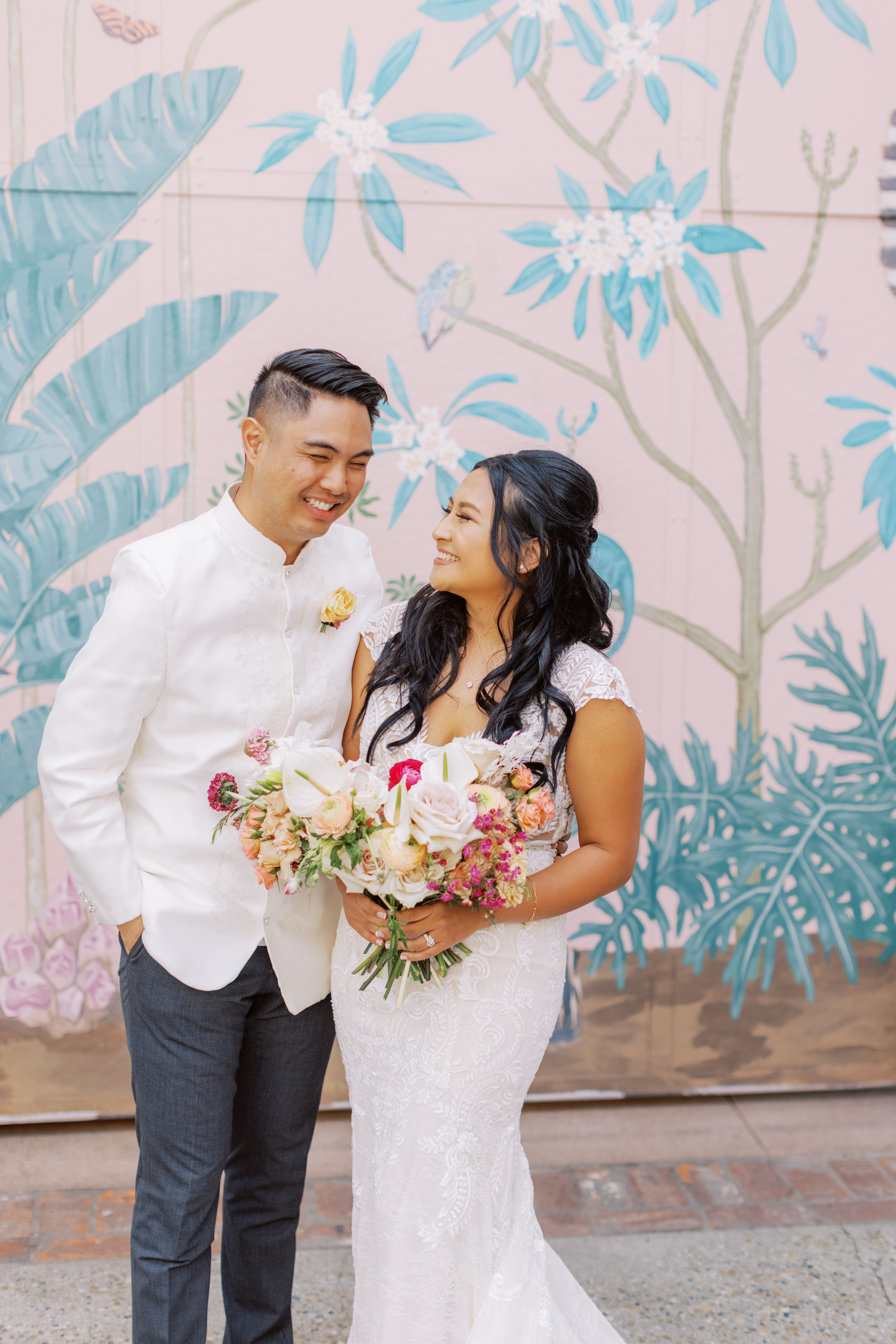 bride in lace dress holding tropical bouquet and groom in white wedding attire pose during cocktail hour at The Valentine DTLA 