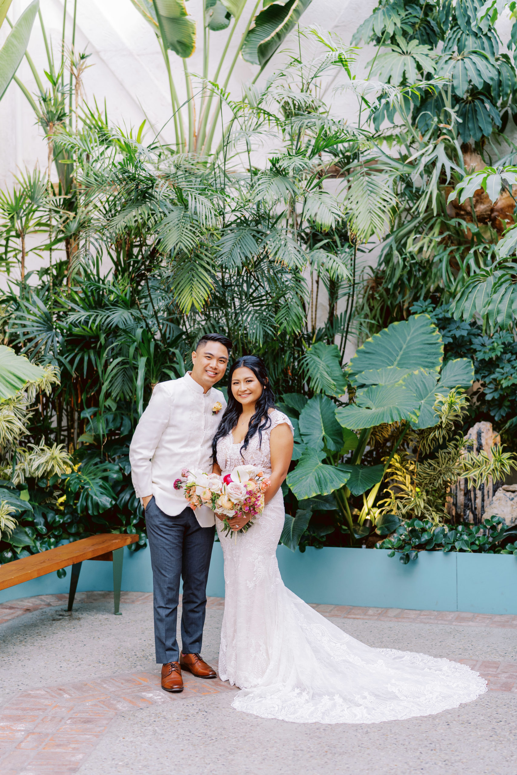 bride in lace dress with bright tropical bouquet poses with groom in white wedding attire during cocktail hour at The Valentine DTLA 