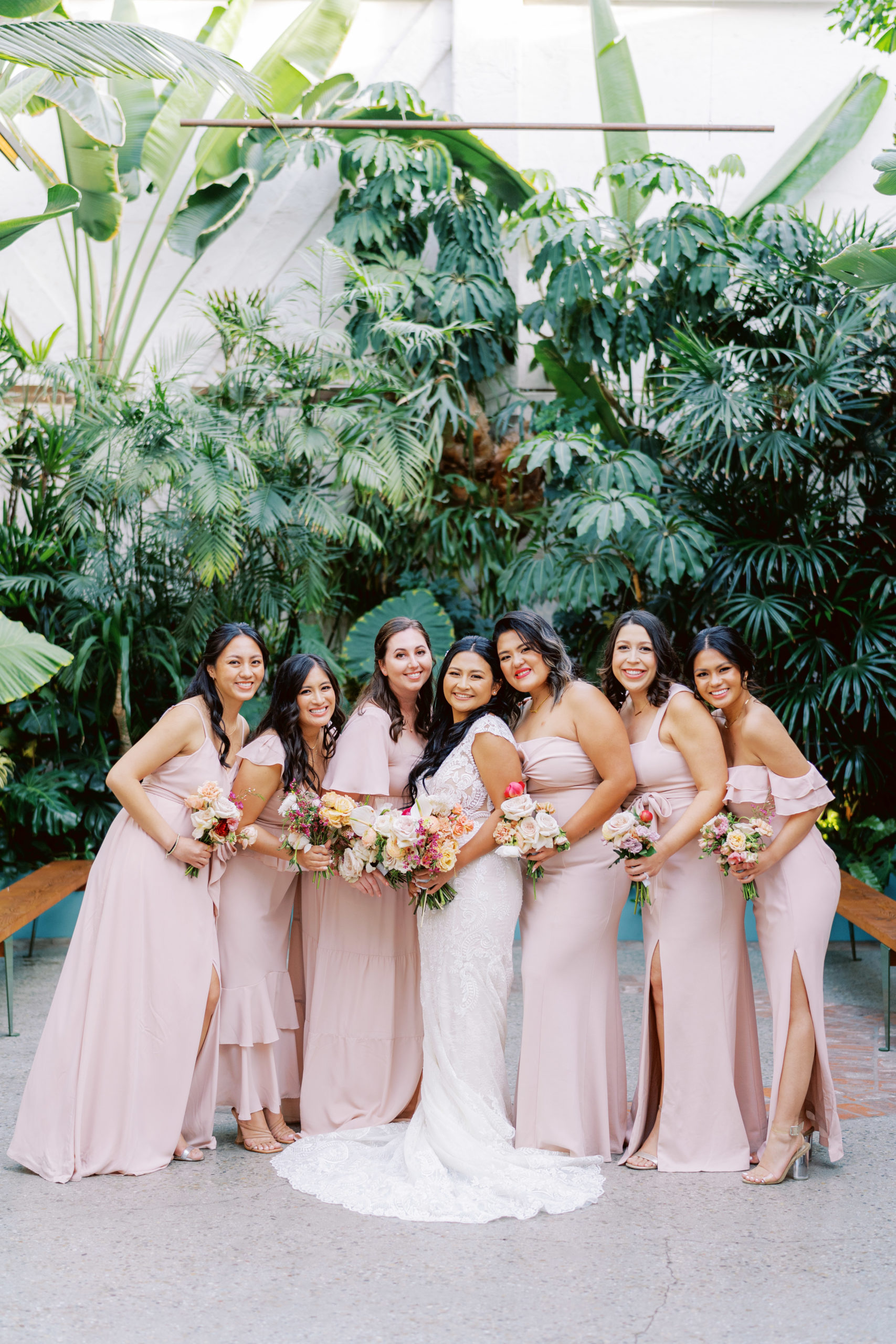 bride in lace dress with bright tropical bouquet poses with bridesmaids in light pink mix matched dresses during cocktail hour at The Valentine DTLA 