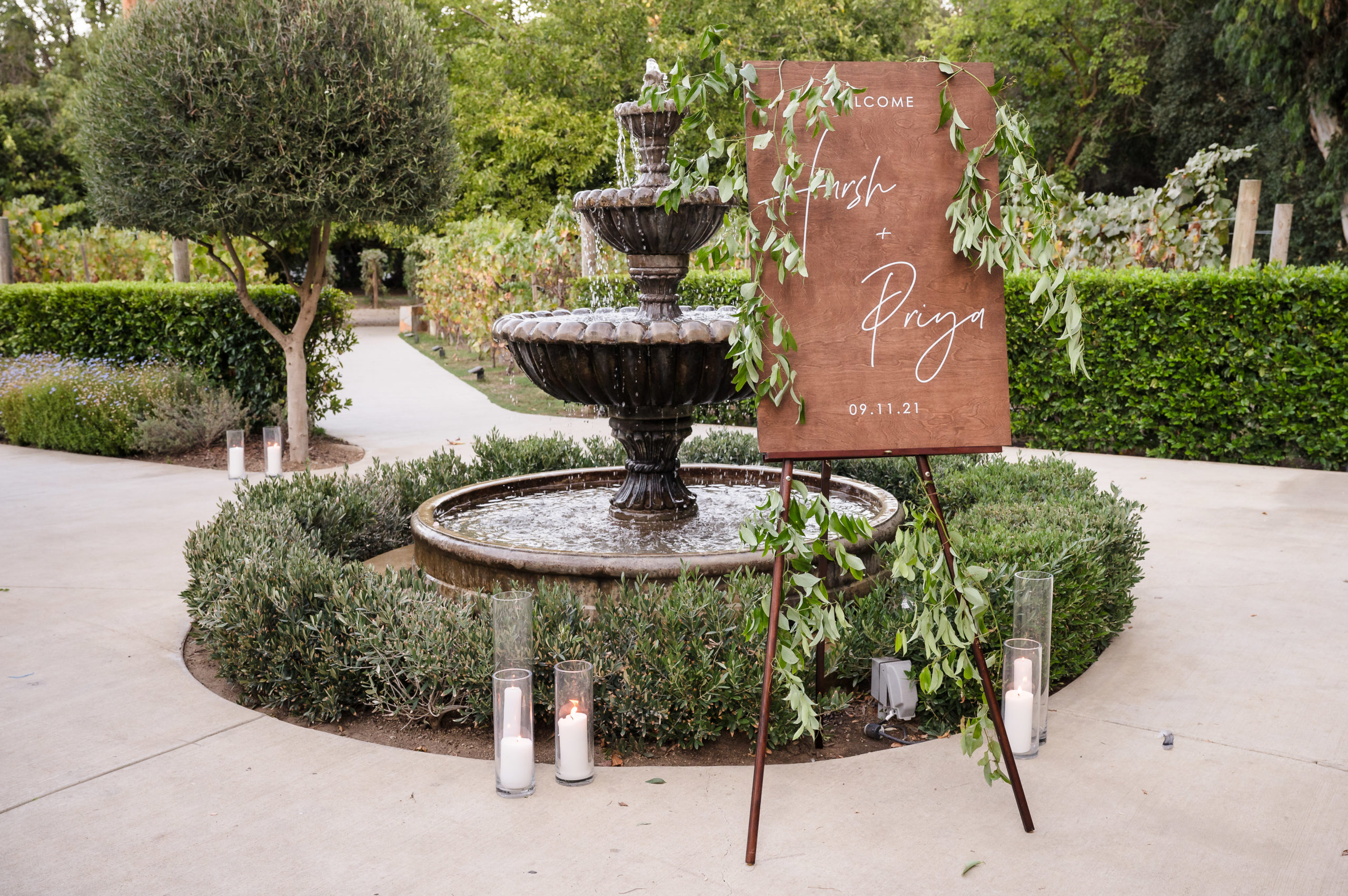 Wooden wedding welcome sign with greenery in front of fountain