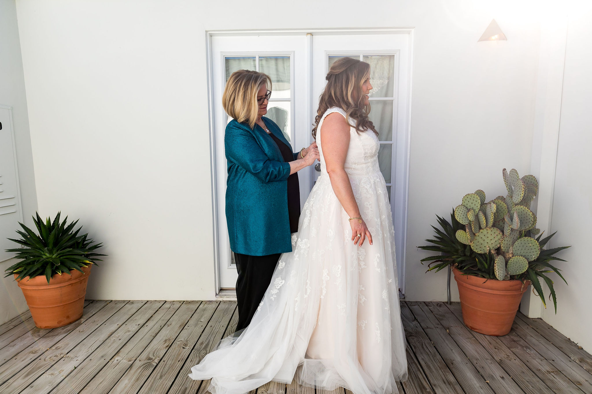 mother of bride helping bride into her lace dress before wedding day