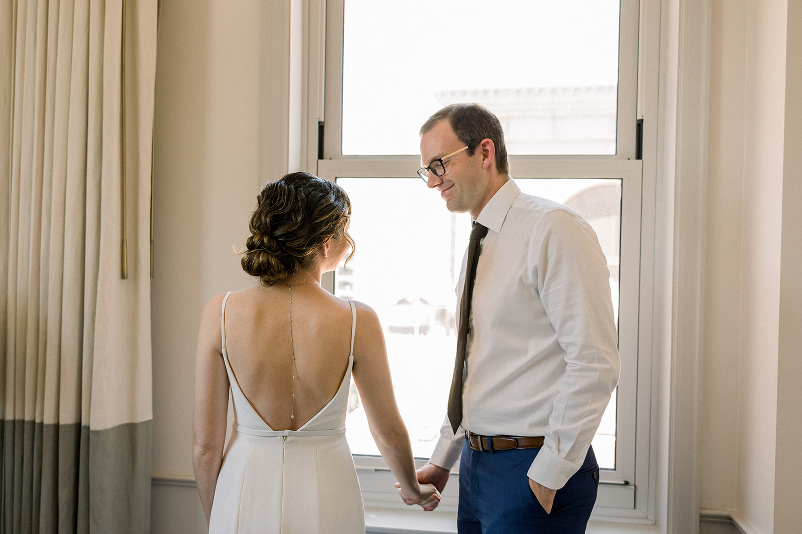 bride in contemporary spaghetti strap dress and low chignon bun kisses groom wearing glasses