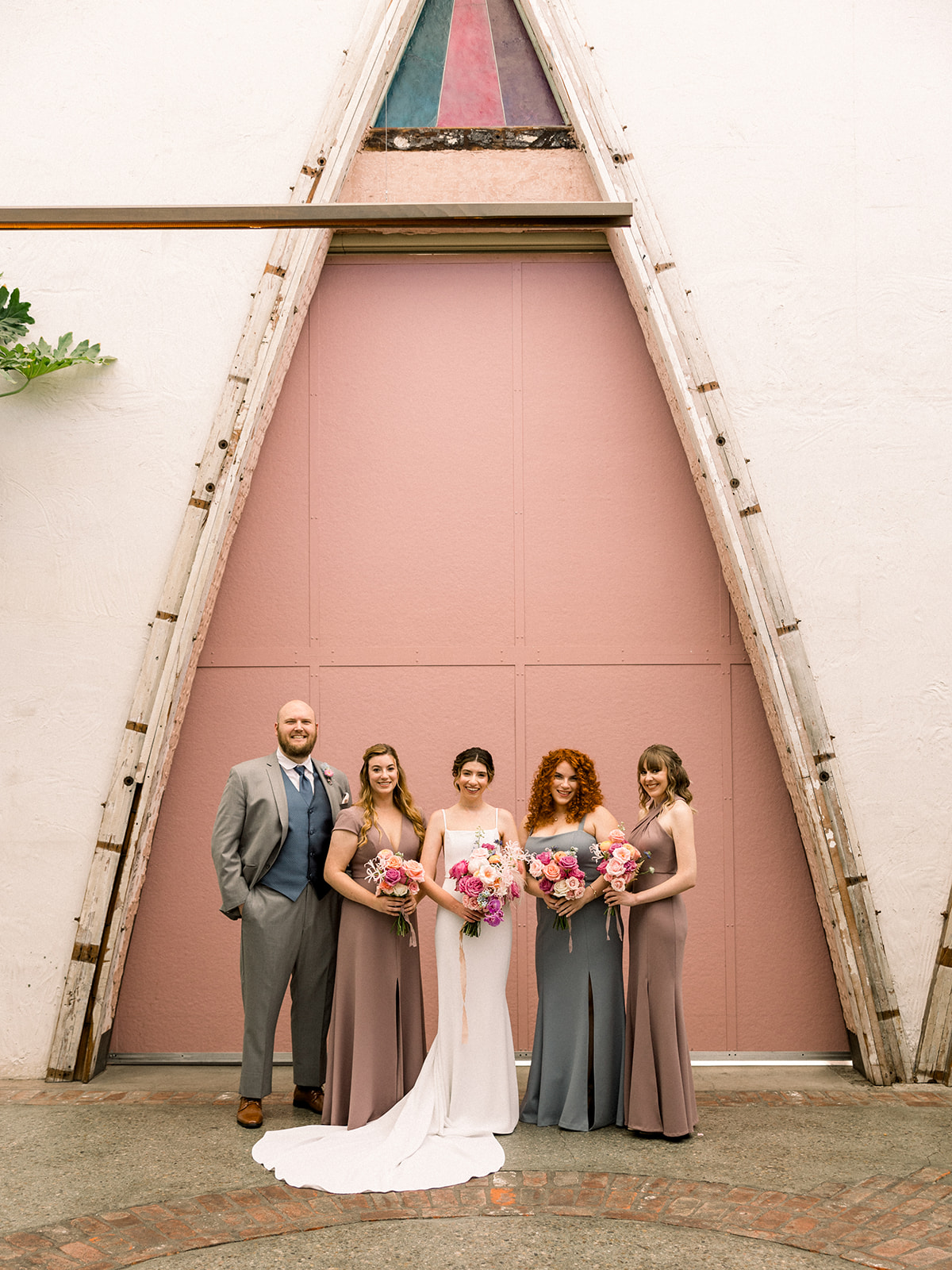 bride in contemporary wedding dress stands with wedding party in muted earth tone dresses and groomsman at The Grassroom DTLA