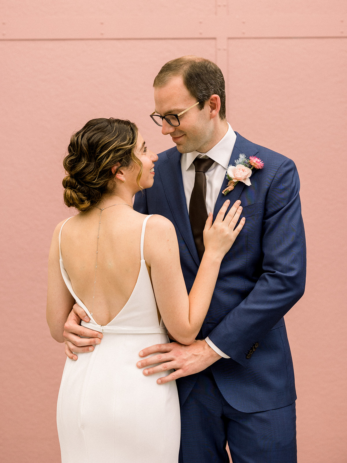 bride in contemporary wedding dress with necklace down the back poses with groom in navy suit