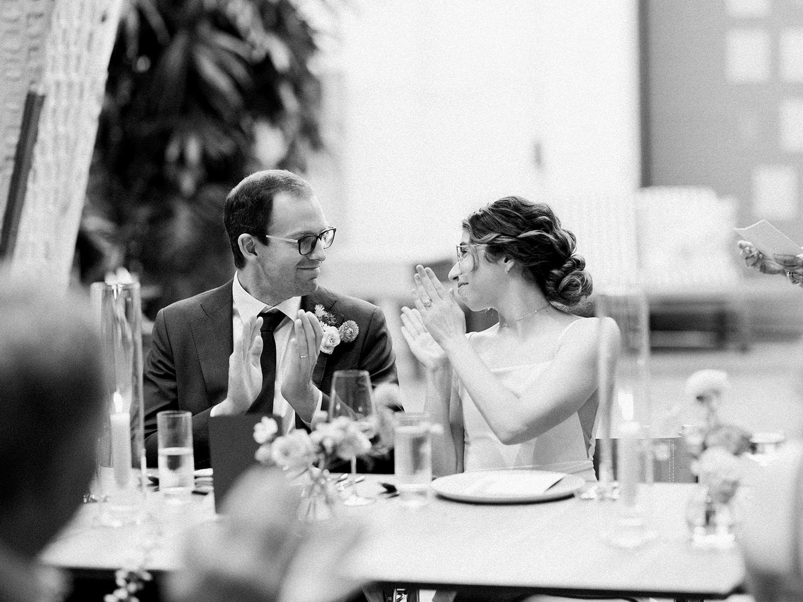 black and white photo of bride and groom wearing glasses looking at each other during wedding reception