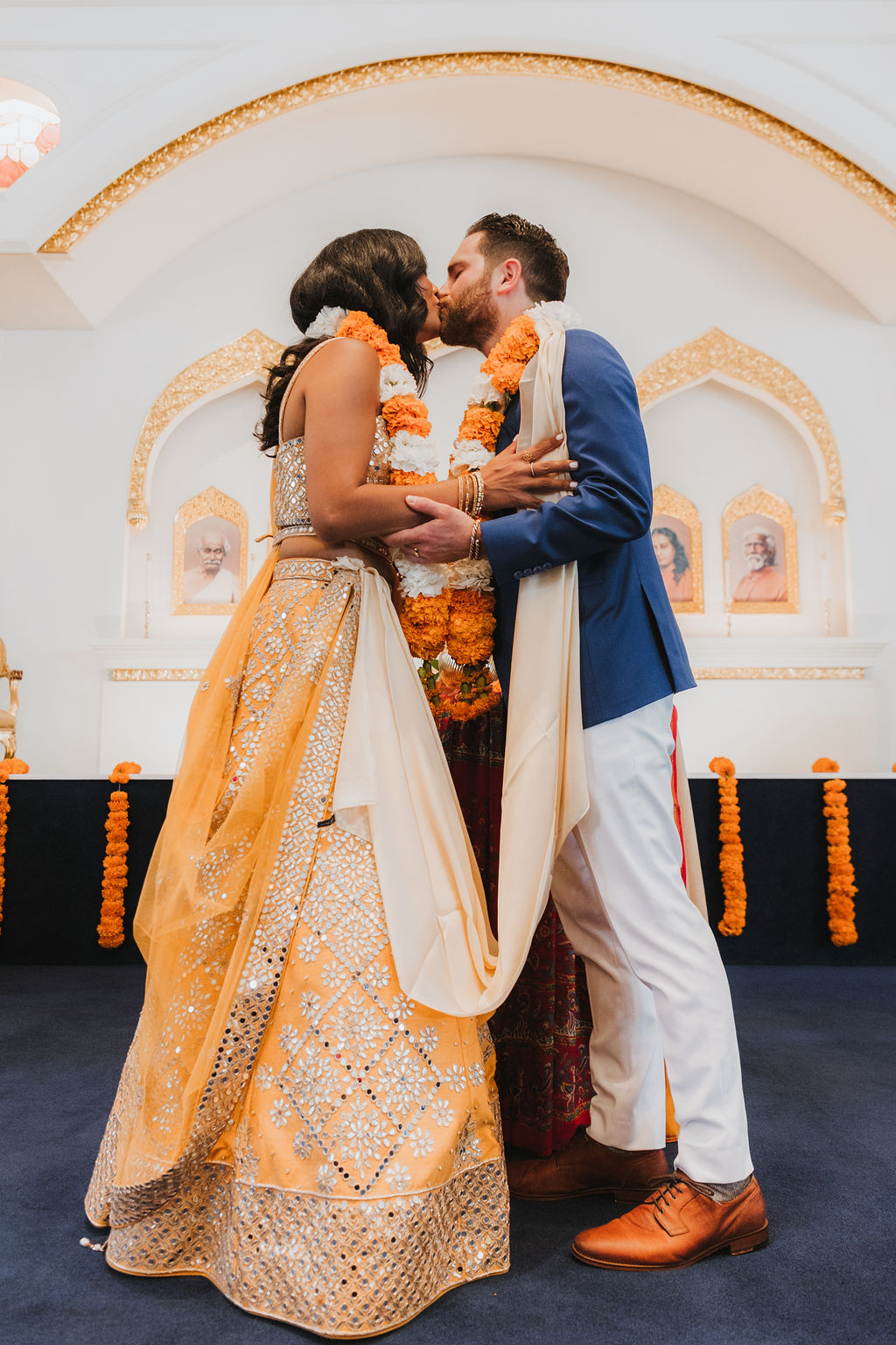bride and groom first kiss during Hindu and Christian wedding ceremony at Lake Shrine Temple in Malibu with orange color palette