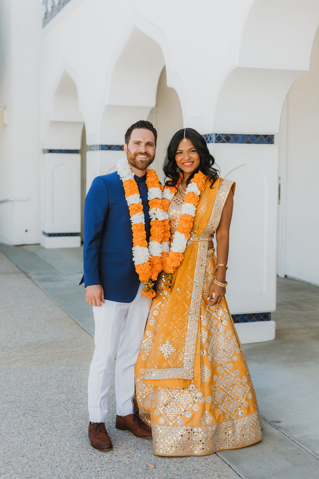 bride in orange sari with groom in cobalt blue suit wearing marigold garland take portrait photos at Lake Shrine Temple in Malibu