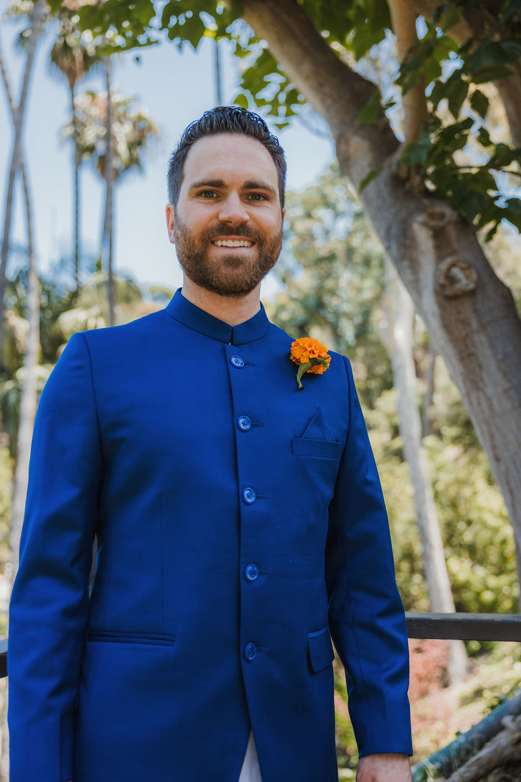 groom in groom with beard wearing cobalt blue suit stands with marigold boutonniere 