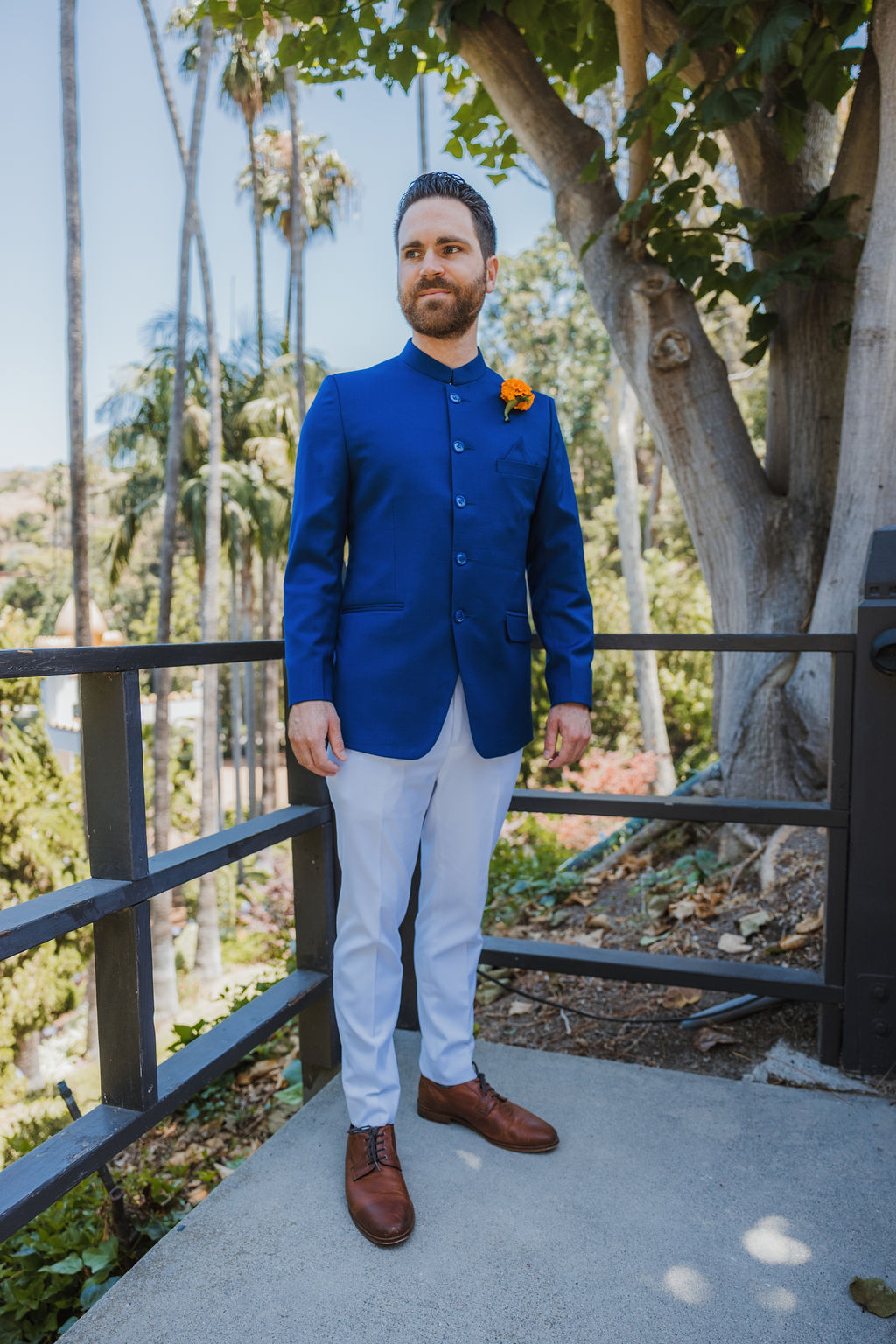 groom in groom with beard wearing cobalt blue suit stands with marigold boutonniere 
