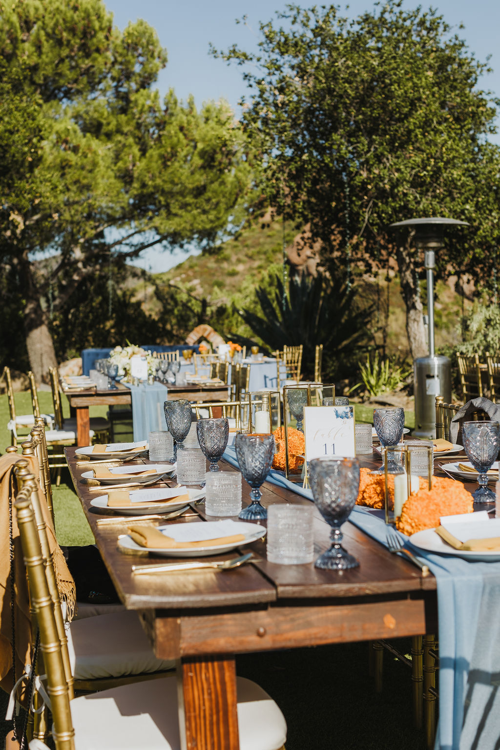 wedding reception at Saddlerock Ranch with orange marigold floral arrangements and blue glassware