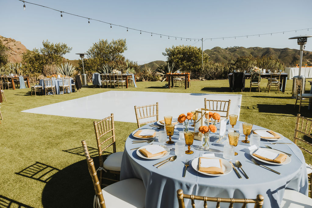 wedding reception at Saddlerock Ranch with orange marigold floral arrangements and blue tablecloth
