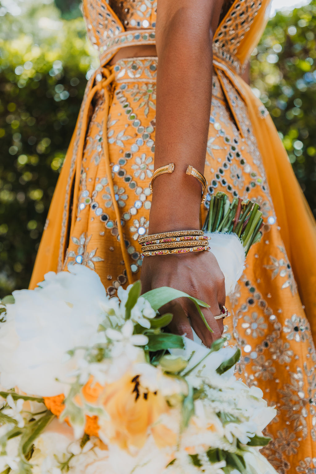 bride in orange marigold colored wedding sari holds bouquet of white and orange flowers
