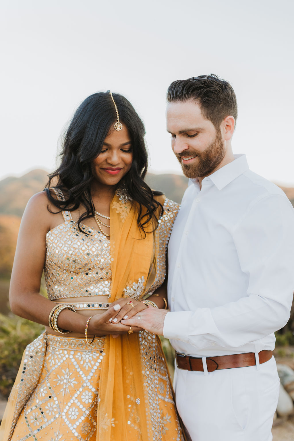 bride in orange sari stands with groom in white during sunset photos at Saddlerock Ranch in Malibu